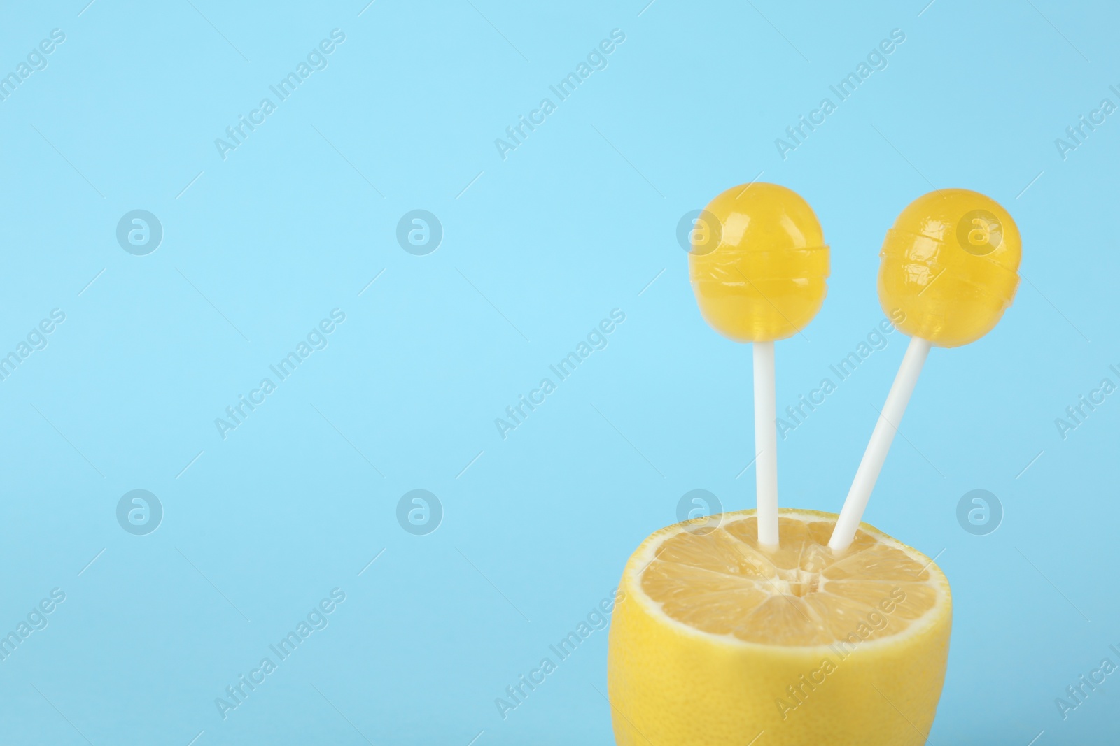 Photo of Fresh lemon with yellow lollipops on light blue background. Space for text