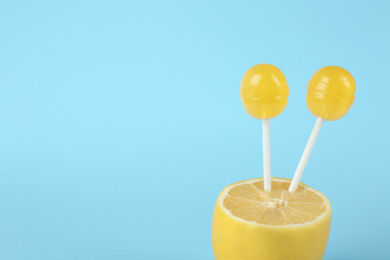 Photo of Fresh lemon with yellow lollipops on light blue background. Space for text