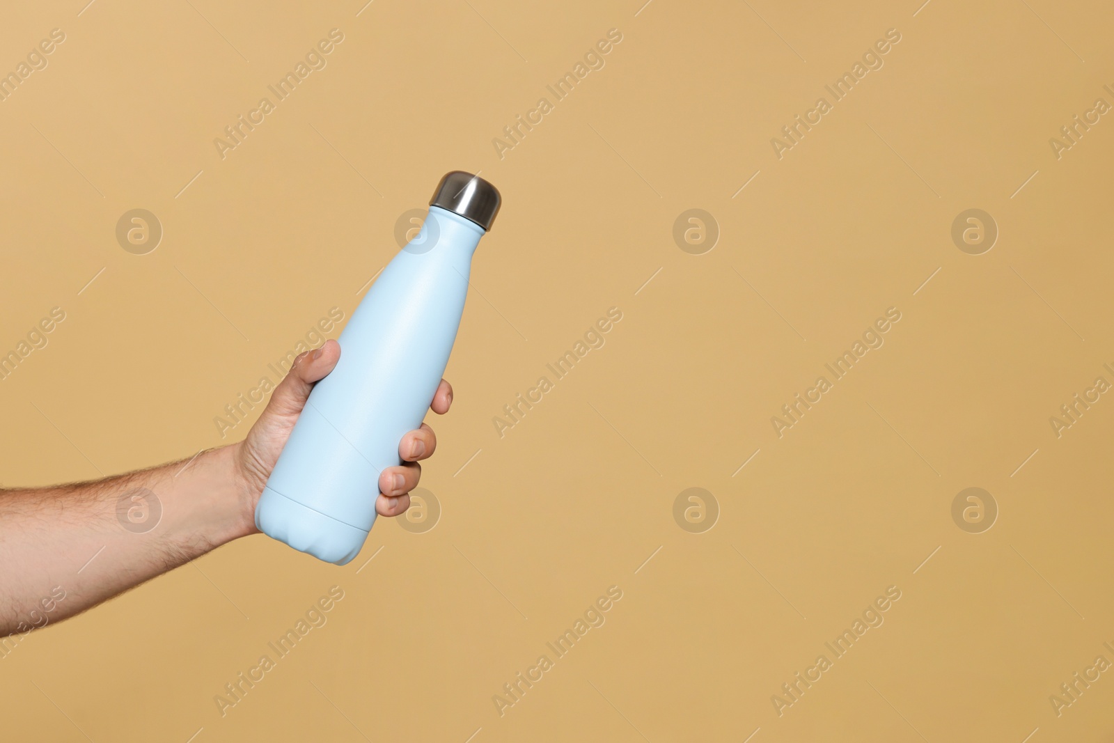 Photo of Man holding thermo bottle on beige background, closeup. Space for text