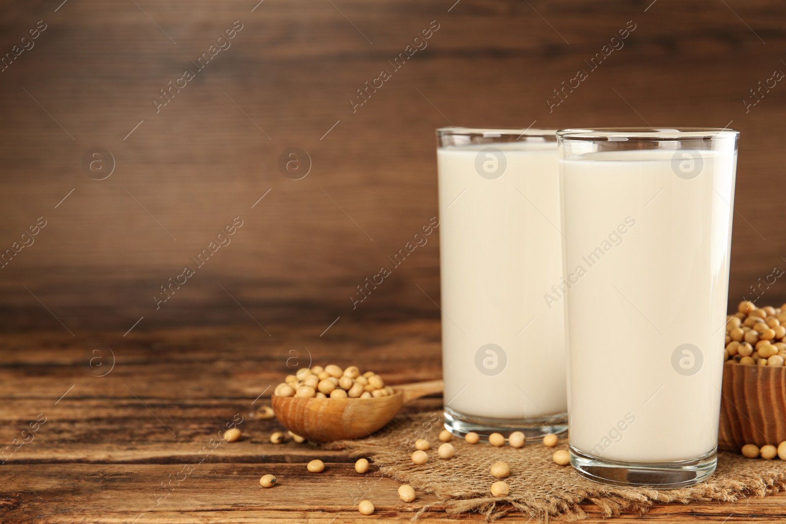 Photo of Glasses with fresh soy milk and grains on wooden table. Space for text