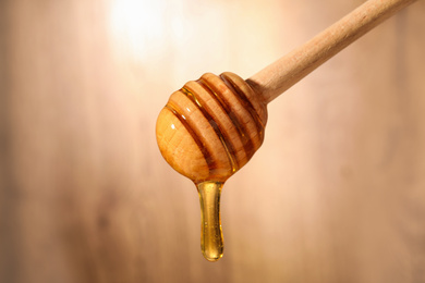 Photo of Dripping honey from wooden dipper on blurred background, closeup