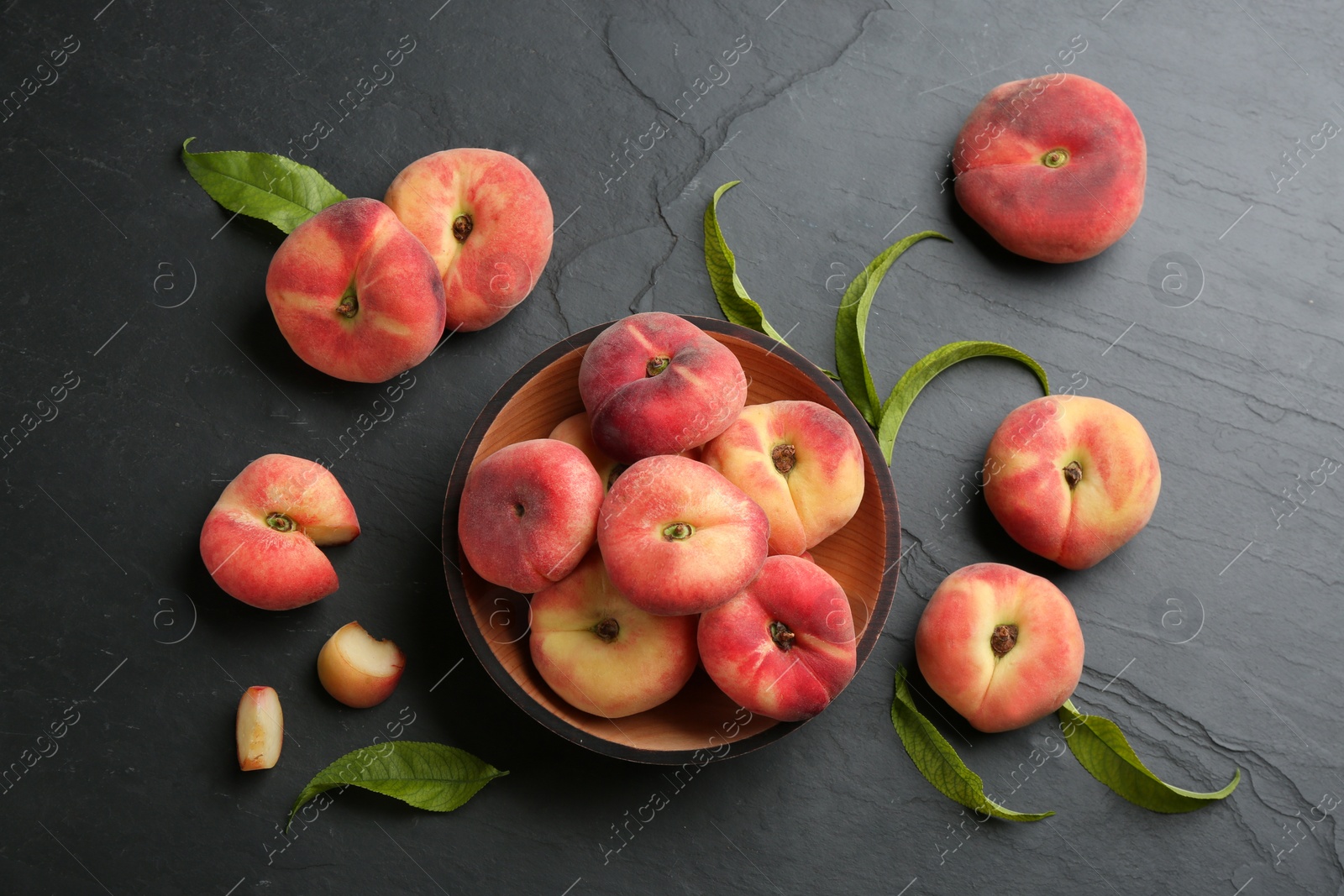 Photo of Fresh ripe donut peaches with leaves on dark table, flat lay