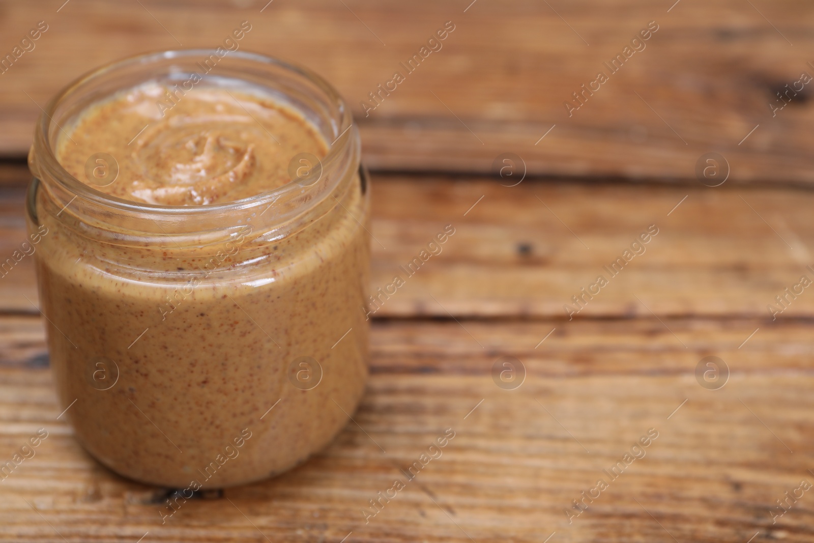 Photo of Tasty nut paste in jar on wooden table, closeup. Space for text