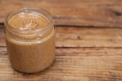 Photo of Tasty nut paste in jar on wooden table, closeup. Space for text