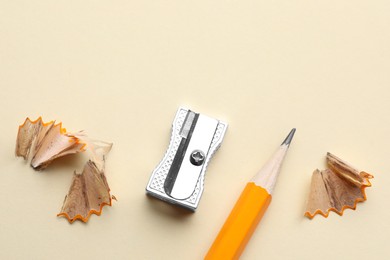 Photo of Pencil, sharpener and shavings on beige background, flat lay. Space for text