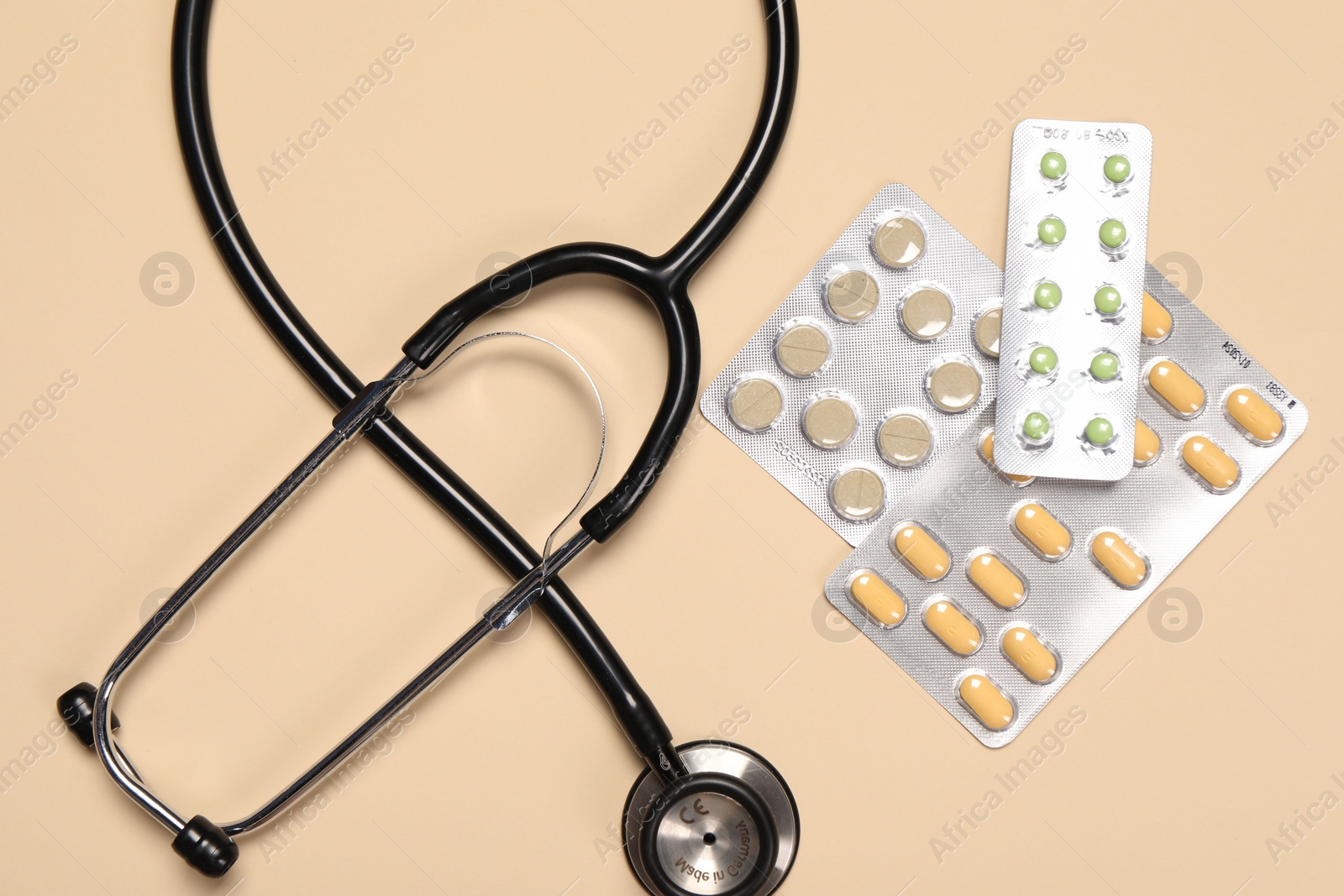 Photo of Stethoscope and pills on beige background, flat lay. Medical tool