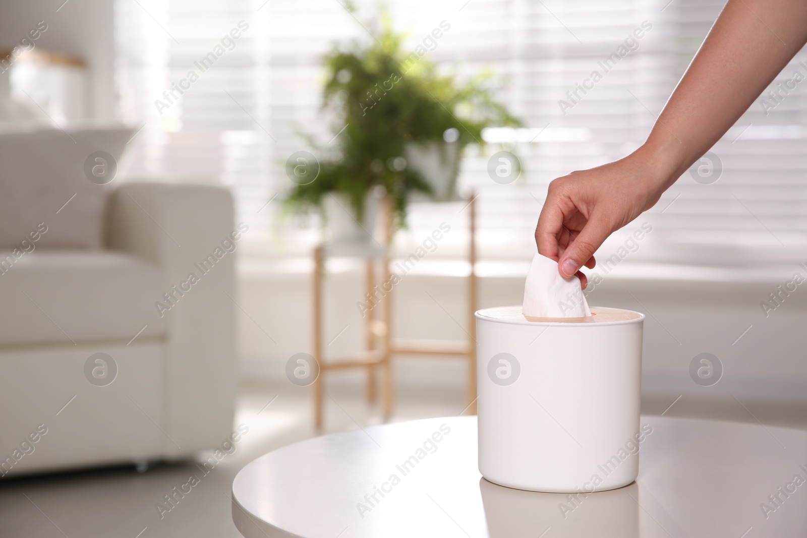 Photo of Woman taking paper tissue out of box on light table at home, closeup. Space for text