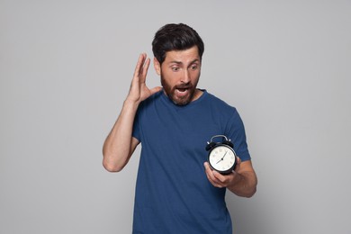 Emotional bearded man with alarm clock on light grey background. Being late concept