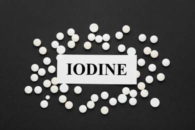 Card with iodine element and pills on black background, flat lay