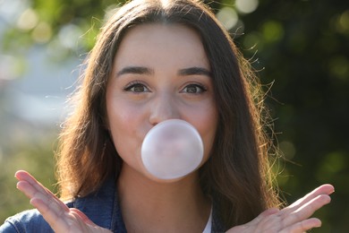 Photo of Beautiful young woman blowing bubble gum outdoors