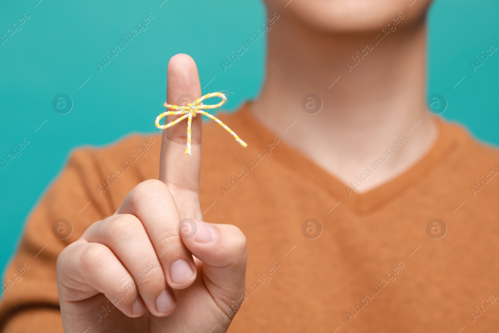 Photo of Man showing index finger with tied bow as reminder against turquoise background, focus on hand