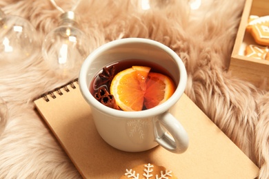 Photo of Cup of hot winter drink and notebook on fluffy plaid. Cozy season