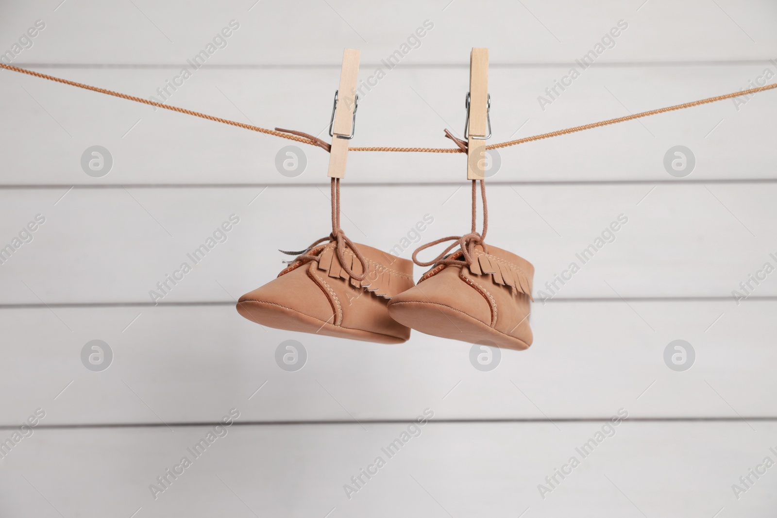 Photo of Cute baby shoes drying on washing line against white wall