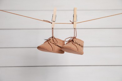 Photo of Cute baby shoes drying on washing line against white wall