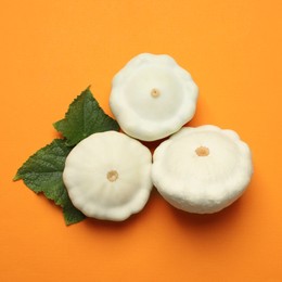 Photo of Fresh ripe pattypan squashes with leaves on orange background, flat lay