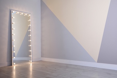 Photo of Large mirror with lamps near color wall. Space for text