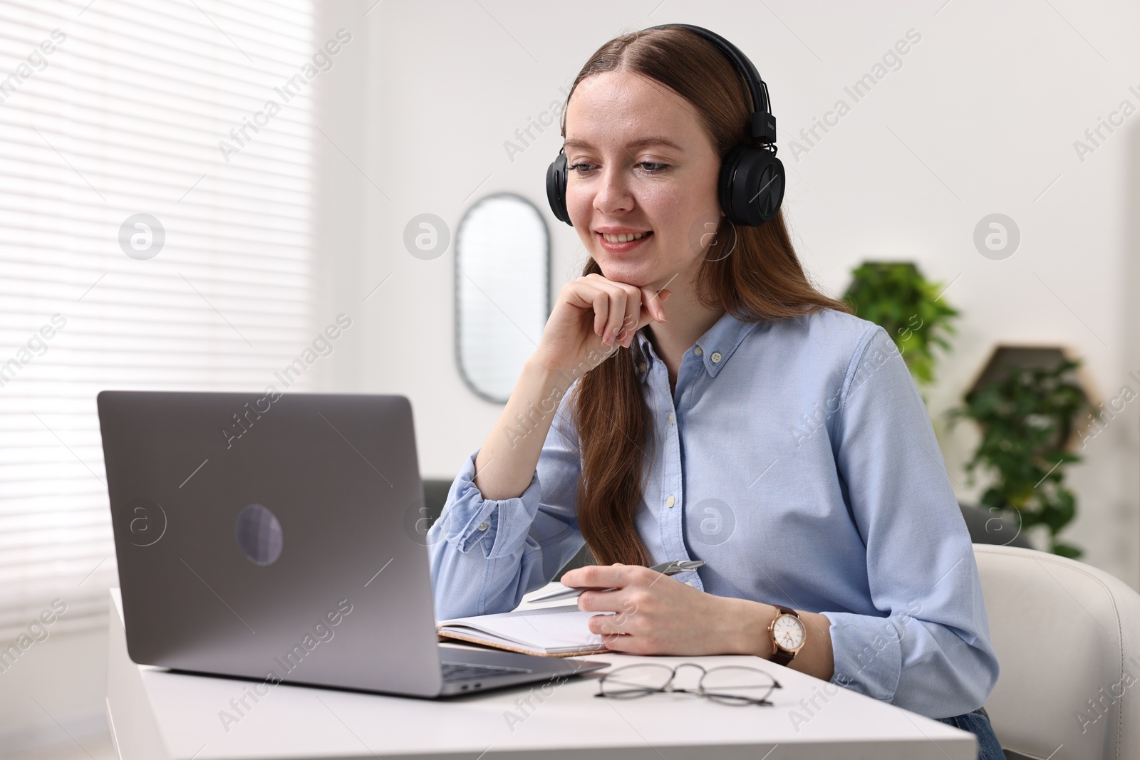 Photo of E-learning. Young woman using laptop during online lesson at white table indoors