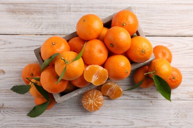 Delicious tangerines with leaves on light wooden table, top view