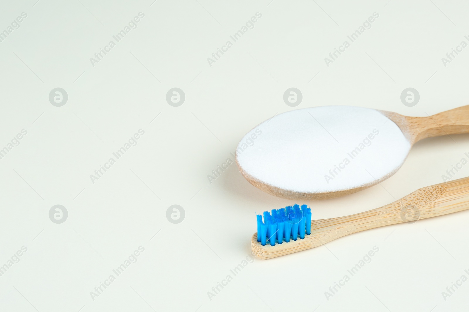 Photo of Bamboo toothbrush and wooden spoon with baking soda on beige background. Space for text