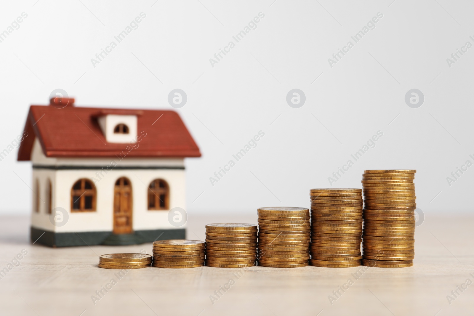 Photo of Mortgage concept. House model and stacks of coins on wooden table against white background, selective focus. Space for text