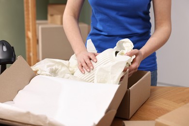 Photo of Post office worker packing parcel at wooden table indoors, closeup