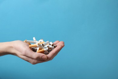 Photo of Stop smoking. Man holding broken cigarettes on light blue background, closeup. Space for text
