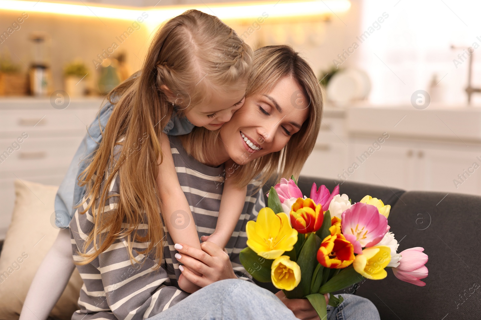 Photo of Little daughter congratulating her mom with Mother`s Day at home. Woman holding bouquet of beautiful tulips