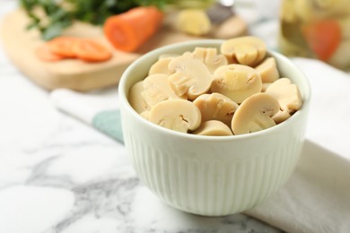 Delicious marinated mushrooms in bowl on white marble table, closeup