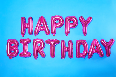 Photo of Phrase HAPPY BIRTHDAY made of pink foil balloon letters on light blue background