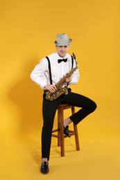 Young man in elegant outfit with saxophone on yellow background