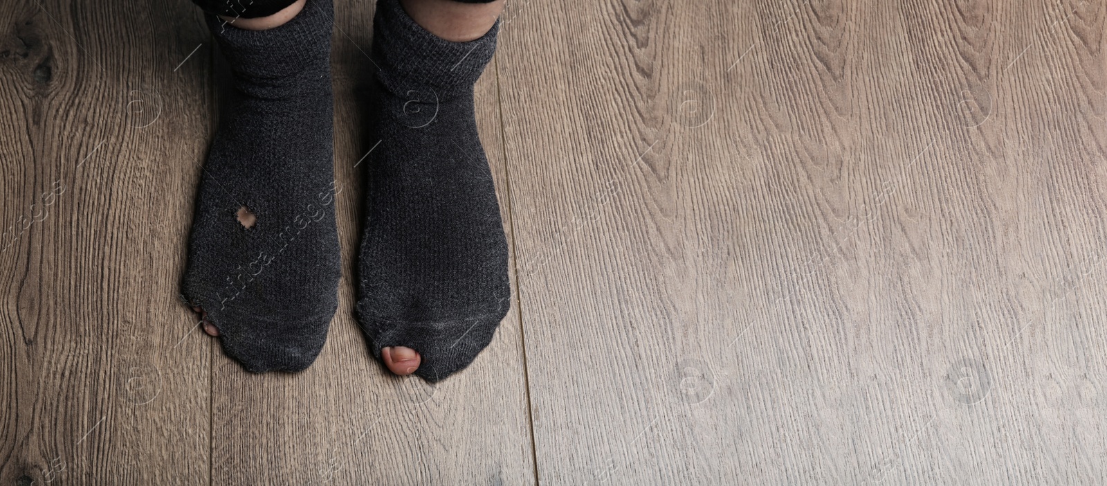 Image of Poor person in shabby socks on wooden floor, closeup view with space for text. Banner design
