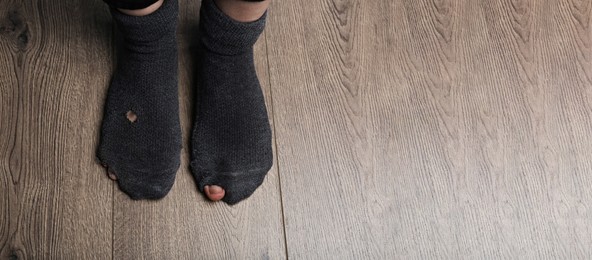 Image of Poor person in shabby socks on wooden floor, closeup view with space for text. Banner design