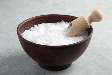 Photo of Natural sea salt in wooden bowl and scoop on light grey marble table