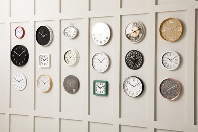 Many different clocks hanging on white wall.