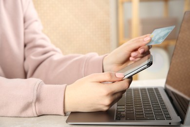 Online payment. Woman using credit card and smartphone near laptop at light grey table indoors, closeup