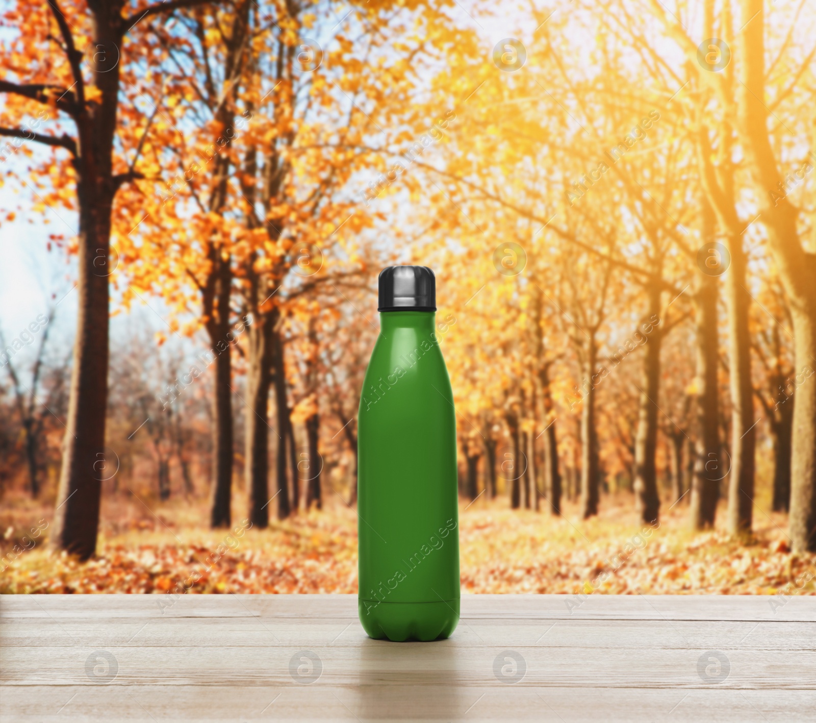 Image of Green thermos bottle on wooden table in autumn park