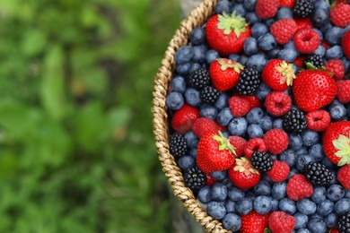 Photo of Wicker bowl with different fresh ripe berries outdoors, top view. Space for text