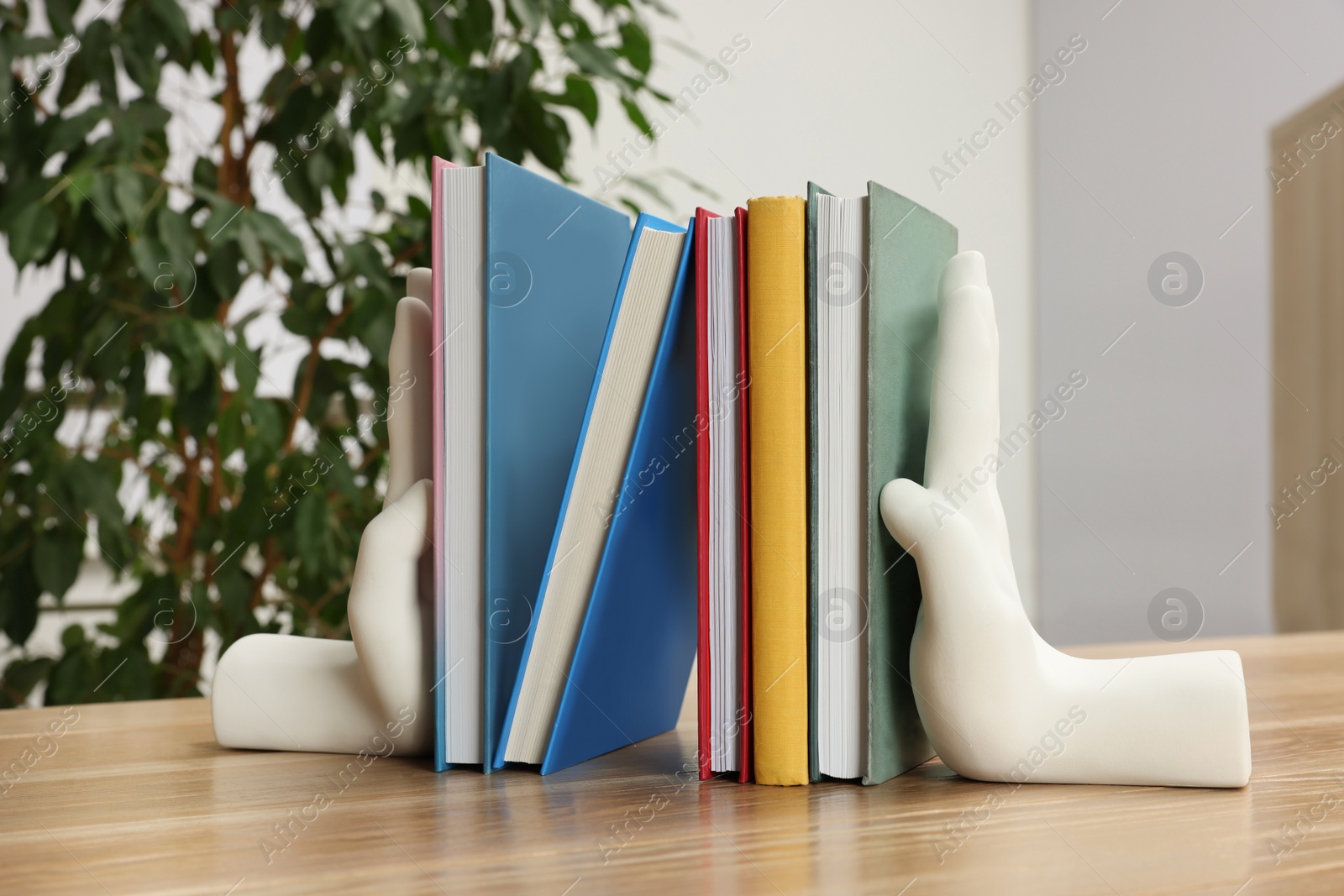 Photo of Beautiful hand shaped bookends with books on wooden table indoors