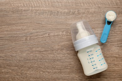 Photo of Feeding bottle with infant formula and powder on wooden table, flat lay. Space for text