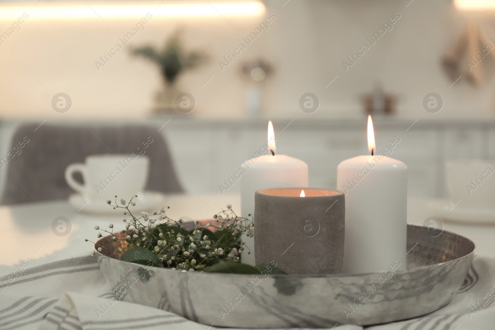 Photo of Beautiful eucalyptus branches, flowers and burning candles on napkin in kitchen. Interior element