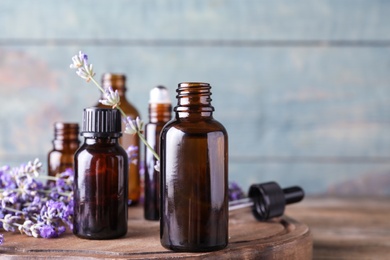 Photo of Bottles of essential oil and lavender flowers on wooden table against blue background. Space for text