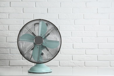 Photo of Electric fan on table near white brick wall, space for text. Summer heat