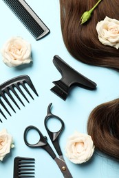 Flat lay composition with professional hairdresser tools, flowers and brown hair strand on light blue background