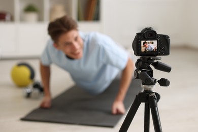 Photo of Smiling sports blogger doing push-ups while recording fitness lesson at home, focus on camera. Space for text