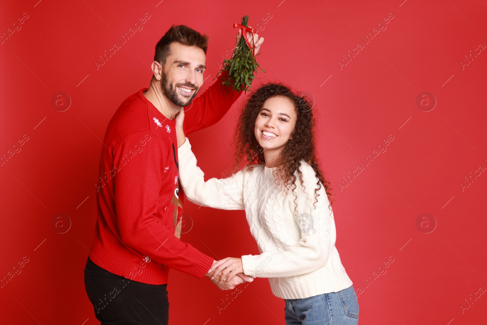 Photo of Portrait of lovely couple under mistletoe bunch on red background