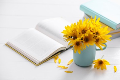 Beautiful bright yellow flowers in light blue cup near books on white table. Space for text