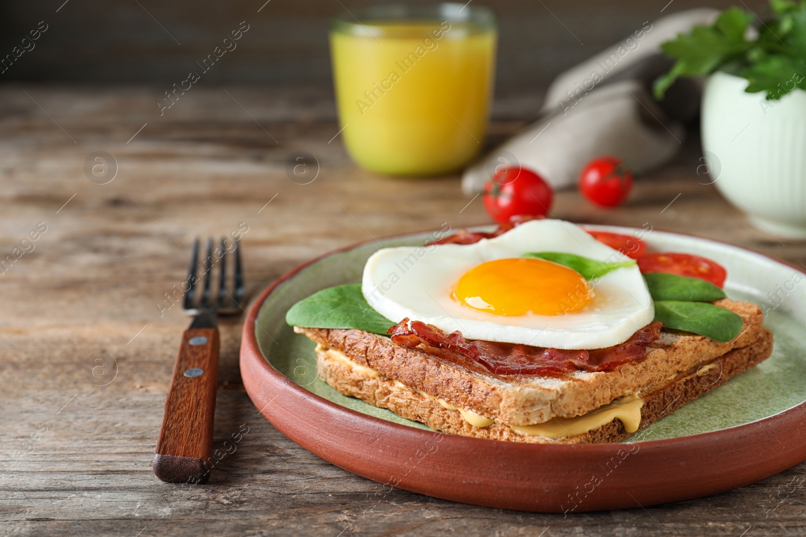 Photo of Plate of tasty sandwich with heart shaped fried egg and  bacon on wooden table, closeup
