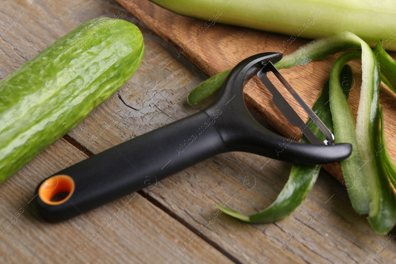 Photo of Fresh cucumbers, peels and peeler on wooden table, closeup