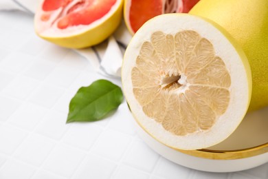 Photo of Tasty pomelo fruits on white tiled table, closeup