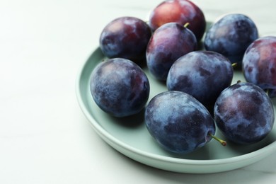 Photo of Plate with tasty ripe plums on white table, closeup